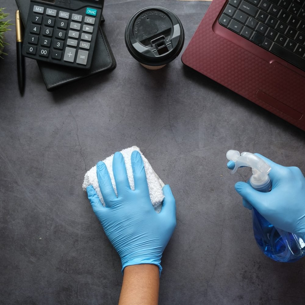 hand in blue rubber gloves holding spray bottle cleaning office table